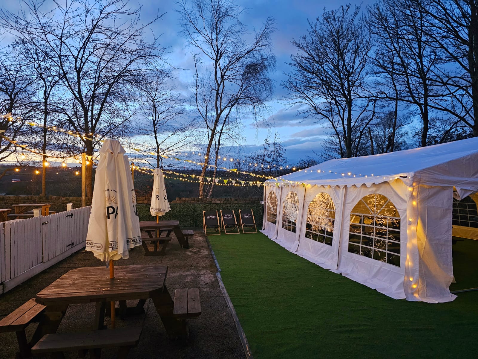 A fairy light lite beer garden with outside seating and a marquee